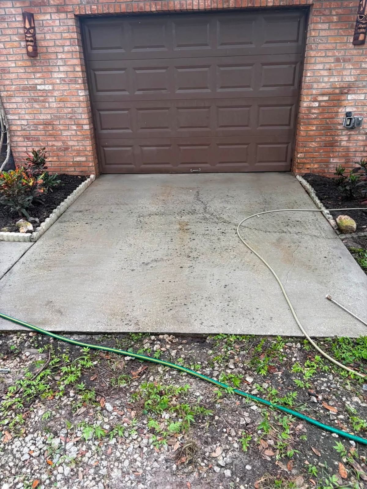 Brown garage door with concrete driveway and garden beds on brick home