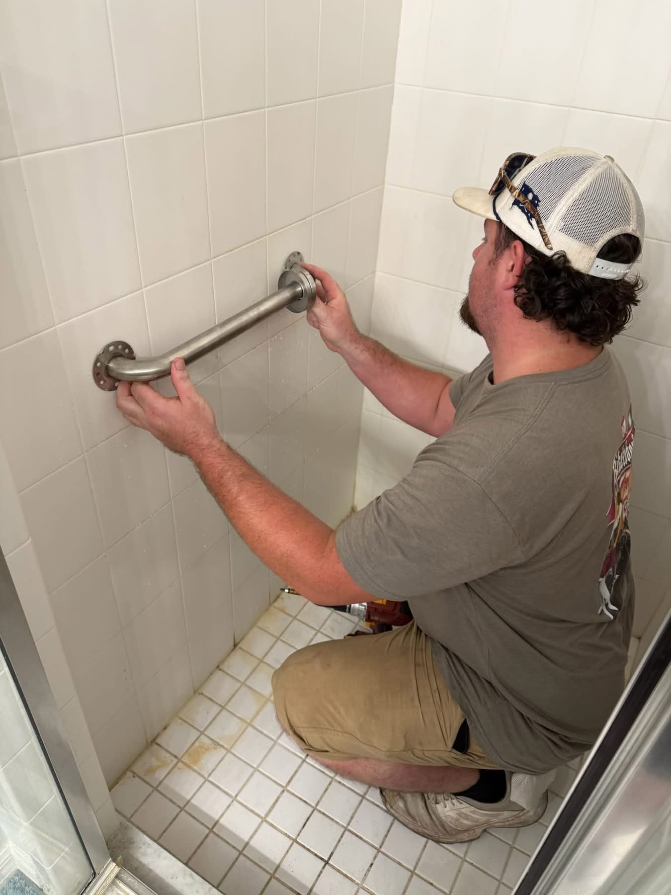 Man installing stainless steel grab bar in bathroom shower wall