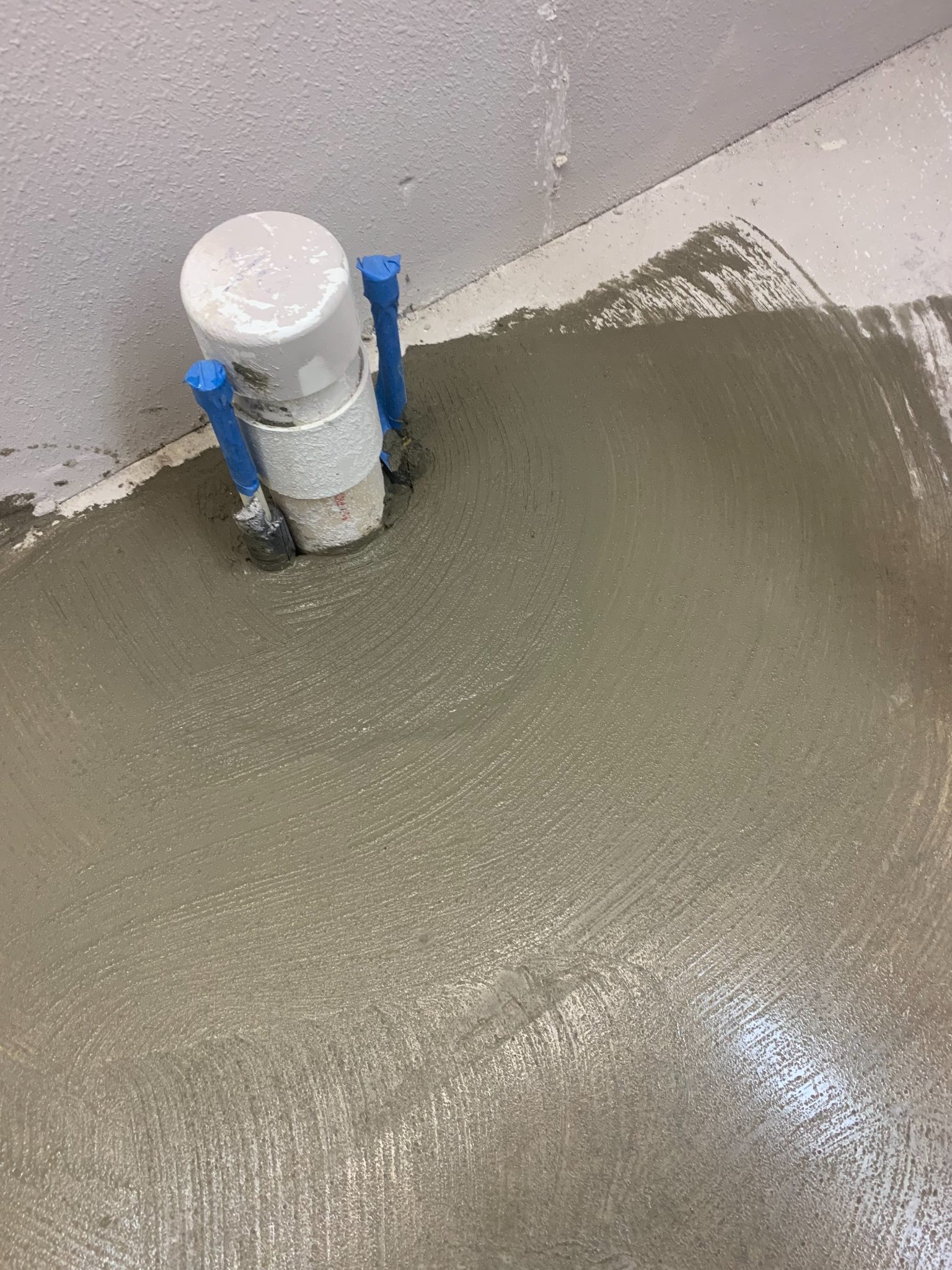 Wet concrete floor being applied with blue-handled tools and white bucket during construction