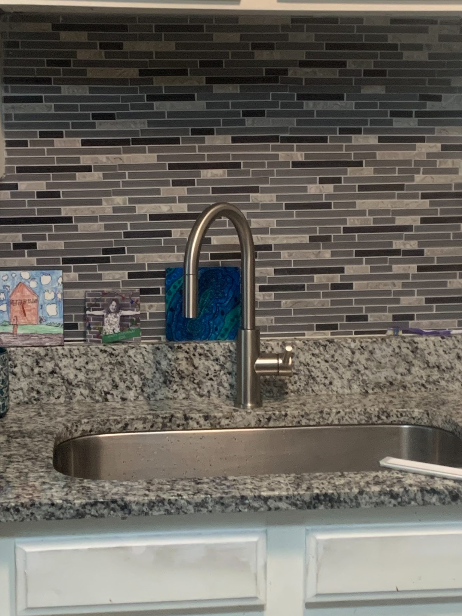 Modern kitchen sink with stainless steel faucet and granite countertop against brick tile backsplash