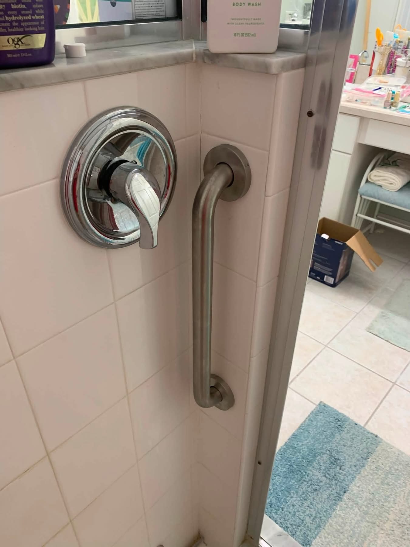 Bathroom shower wall with chrome showerhead and grab bar against pink tile