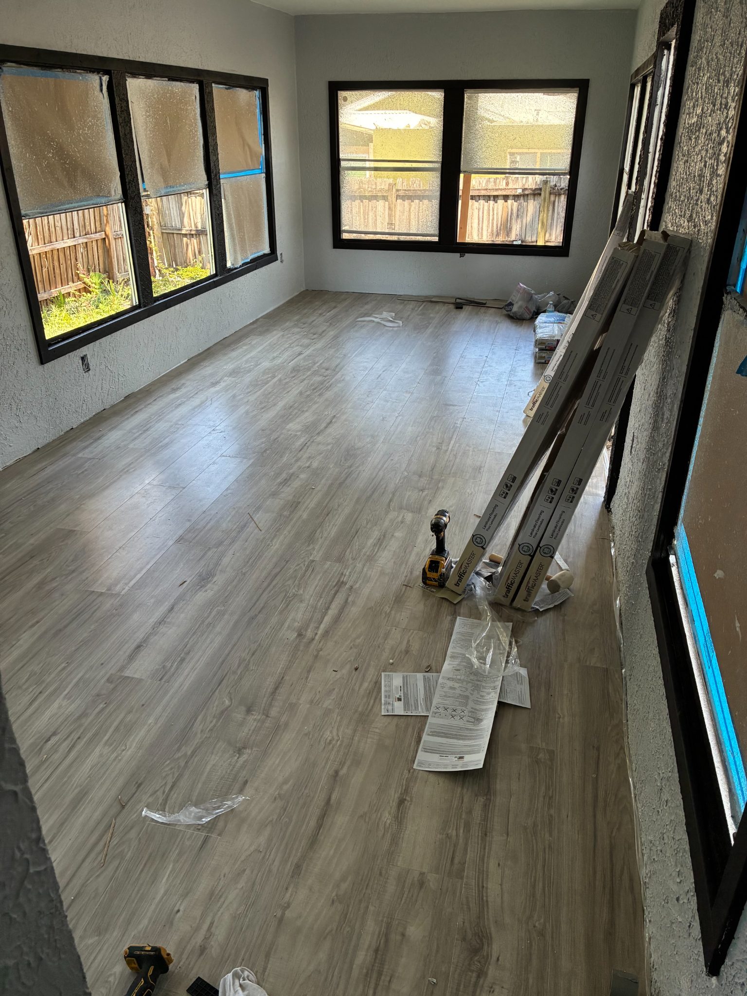 Empty room with wood-grain flooring, black-framed windows, and installation materials stacked along the wall