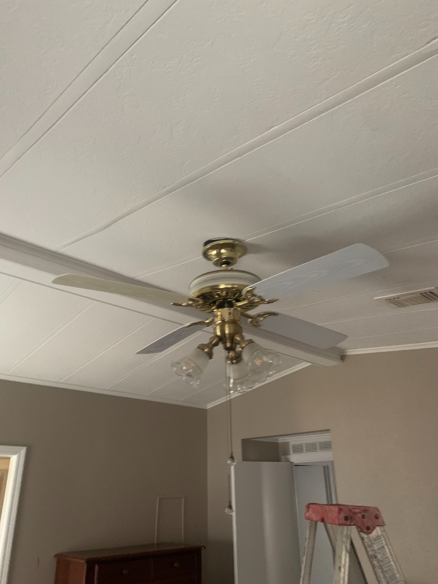 Brass ceiling fan with white blades mounted on drop ceiling in residential room