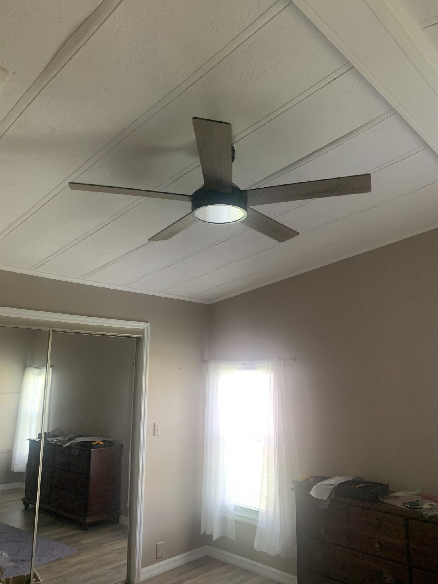 Modern ceiling fan with LED light installed on white coffered ceiling in bedroom