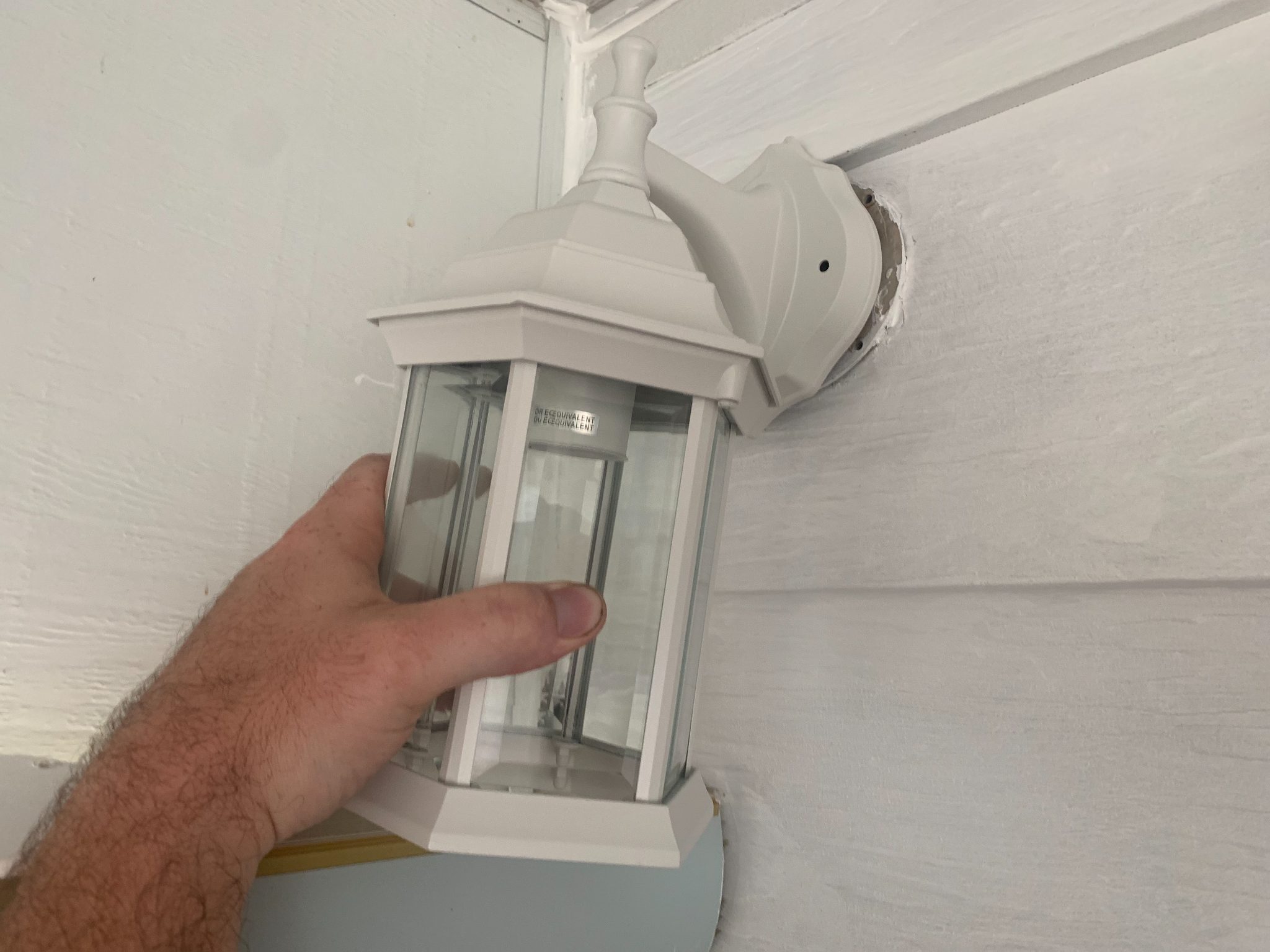 Hand installing white outdoor motion-sensor light fixture on ceiling
