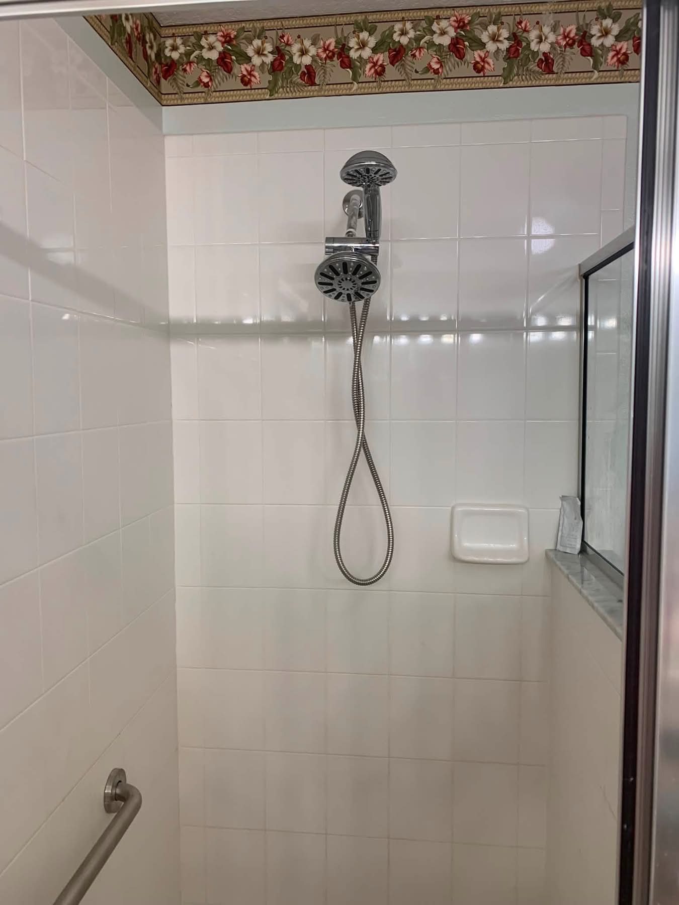 Shower interior with chrome rainfall showerhead and handheld spray on white subway tile walls
