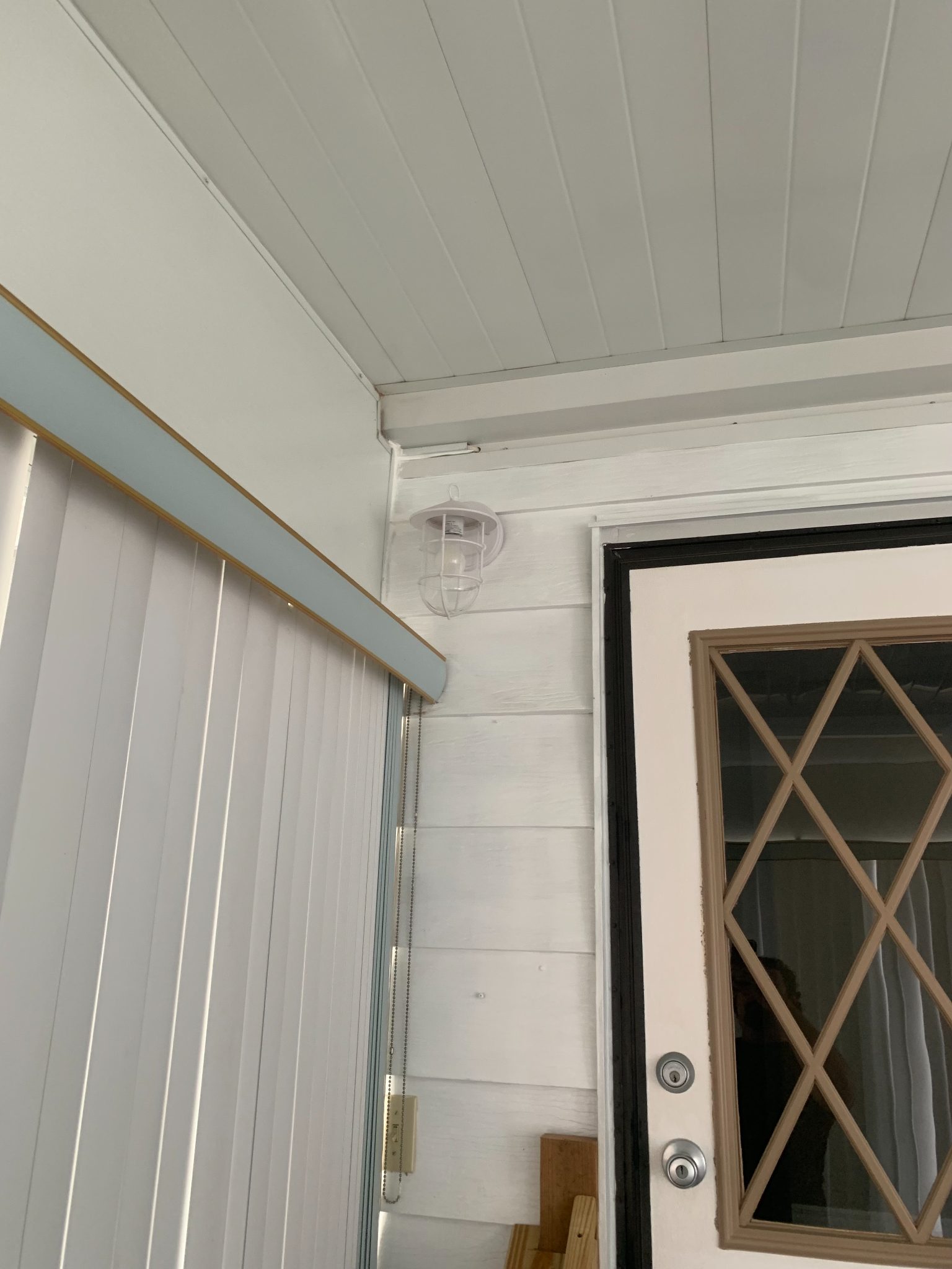 Interior covered porch with white shiplap ceiling, vertical blinds, and glass door with X-pattern frame