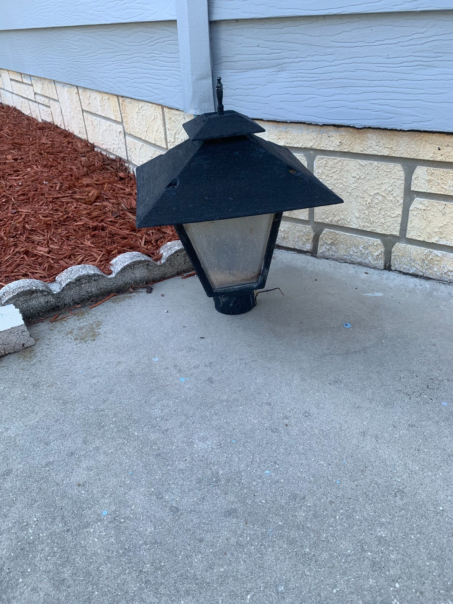 Black outdoor lantern-style wall light mounted on stone foundation near blue siding