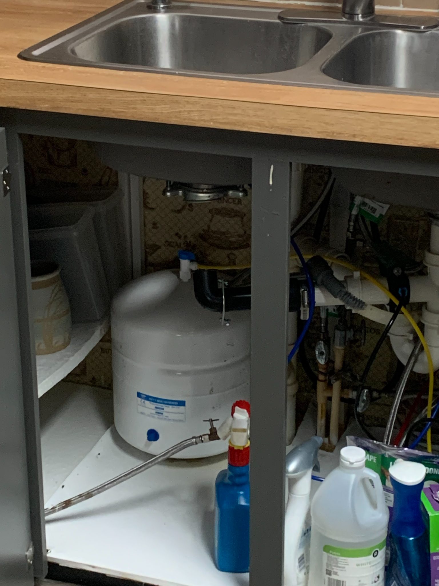 Under-sink cabinet with white water heater, plumbing connections, and cleaning supplies