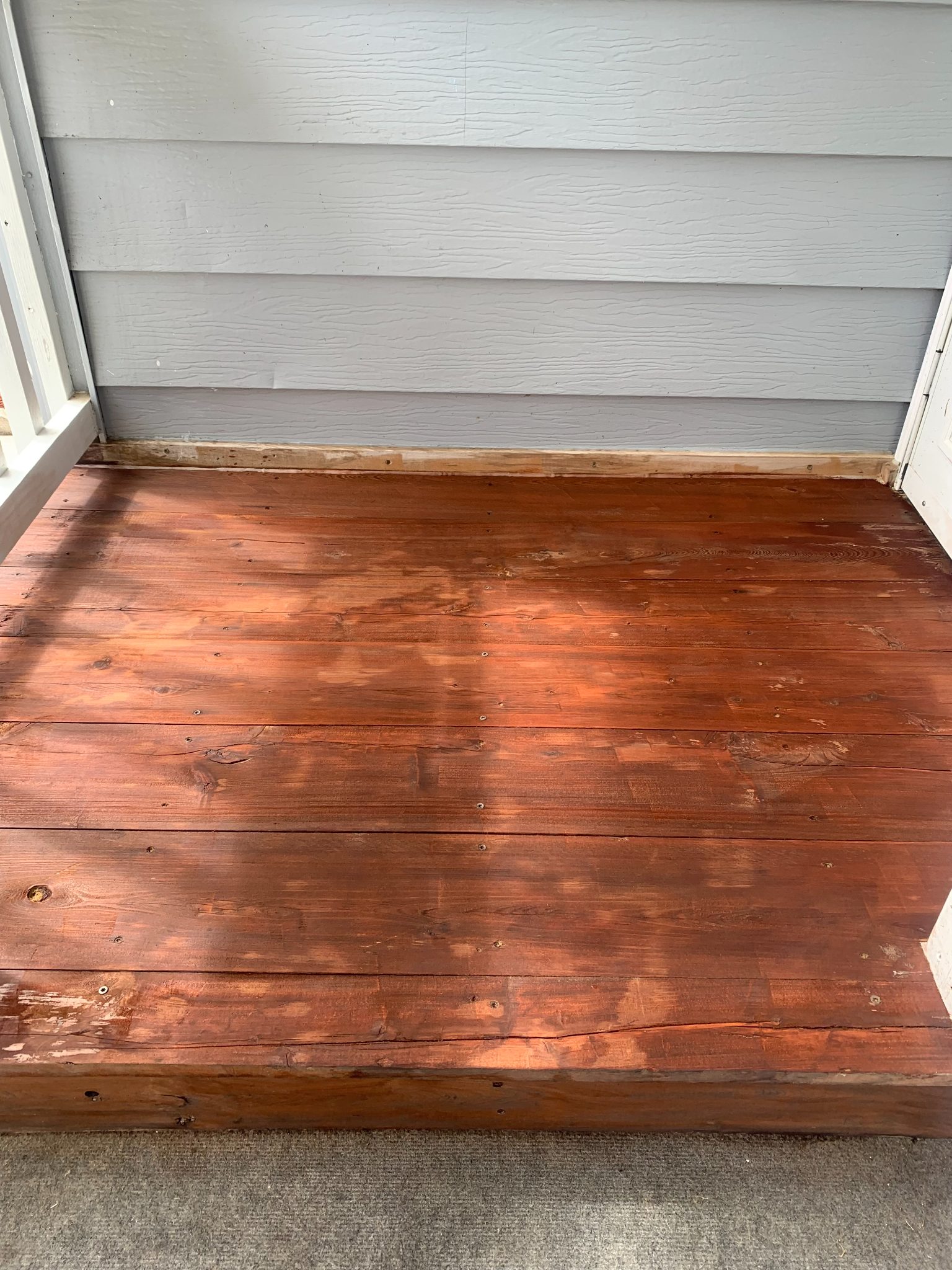 Wooden deck with reddish-brown stain next to gray horizontal siding on house exterior