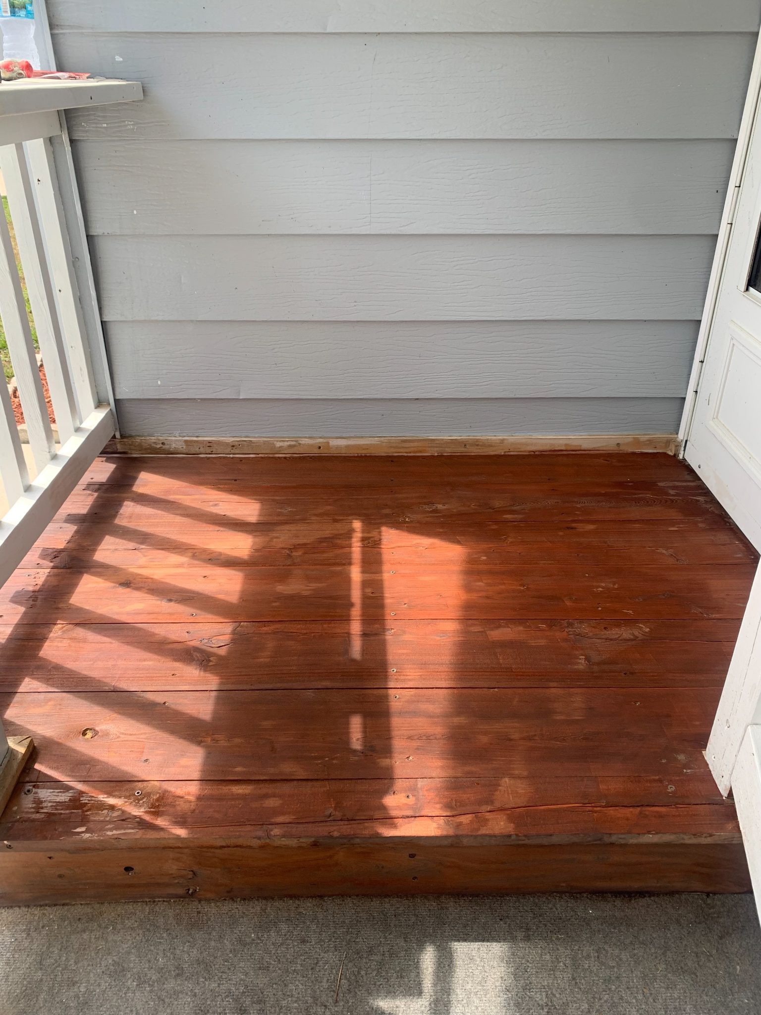 Wooden deck with gray siding wall and white door frame in sunlight
