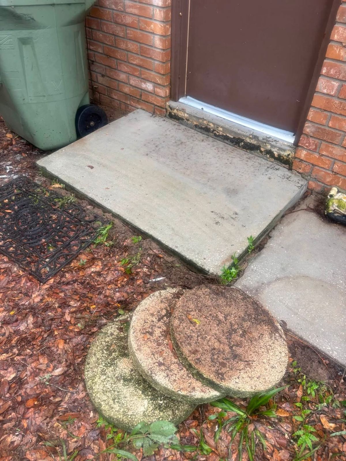 Concrete step and pavers outside brick building entrance with moss and algae growth