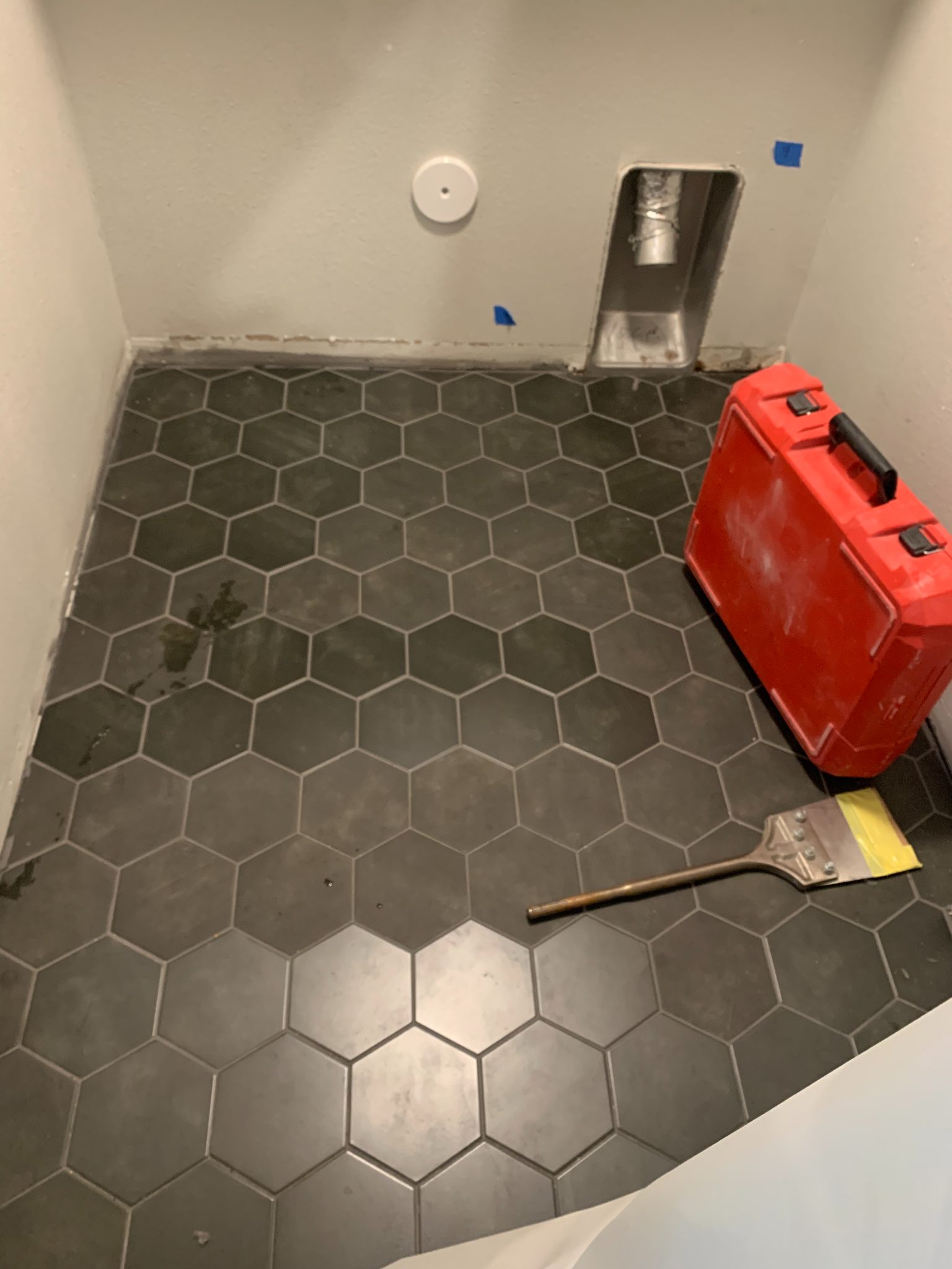 Bathroom under renovation with hexagonal tile flooring, red equipment, paintbrush, and wall-mounted fixtures