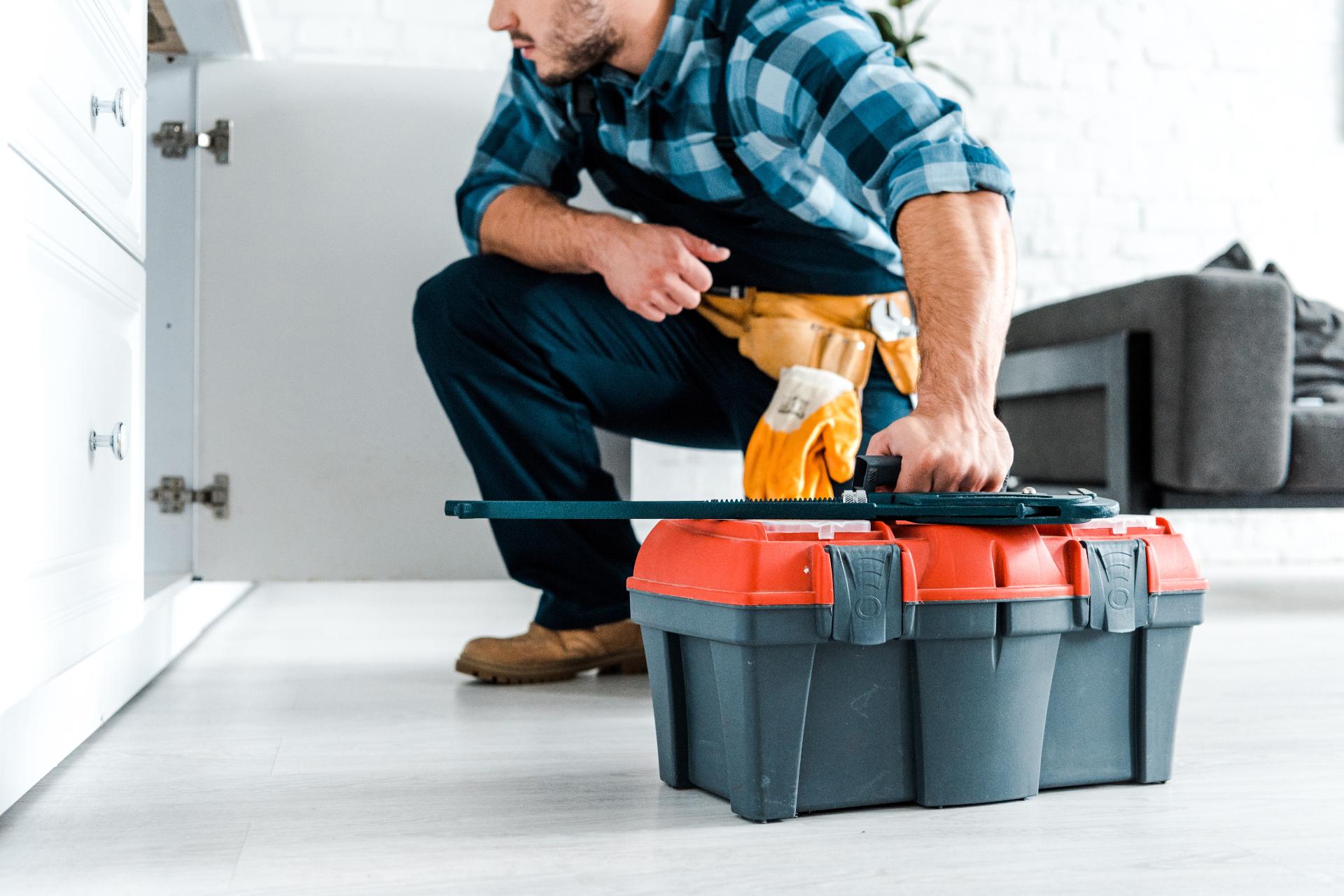 Handyman in blue plaid shirt opening red and gray toolbox in kitchen