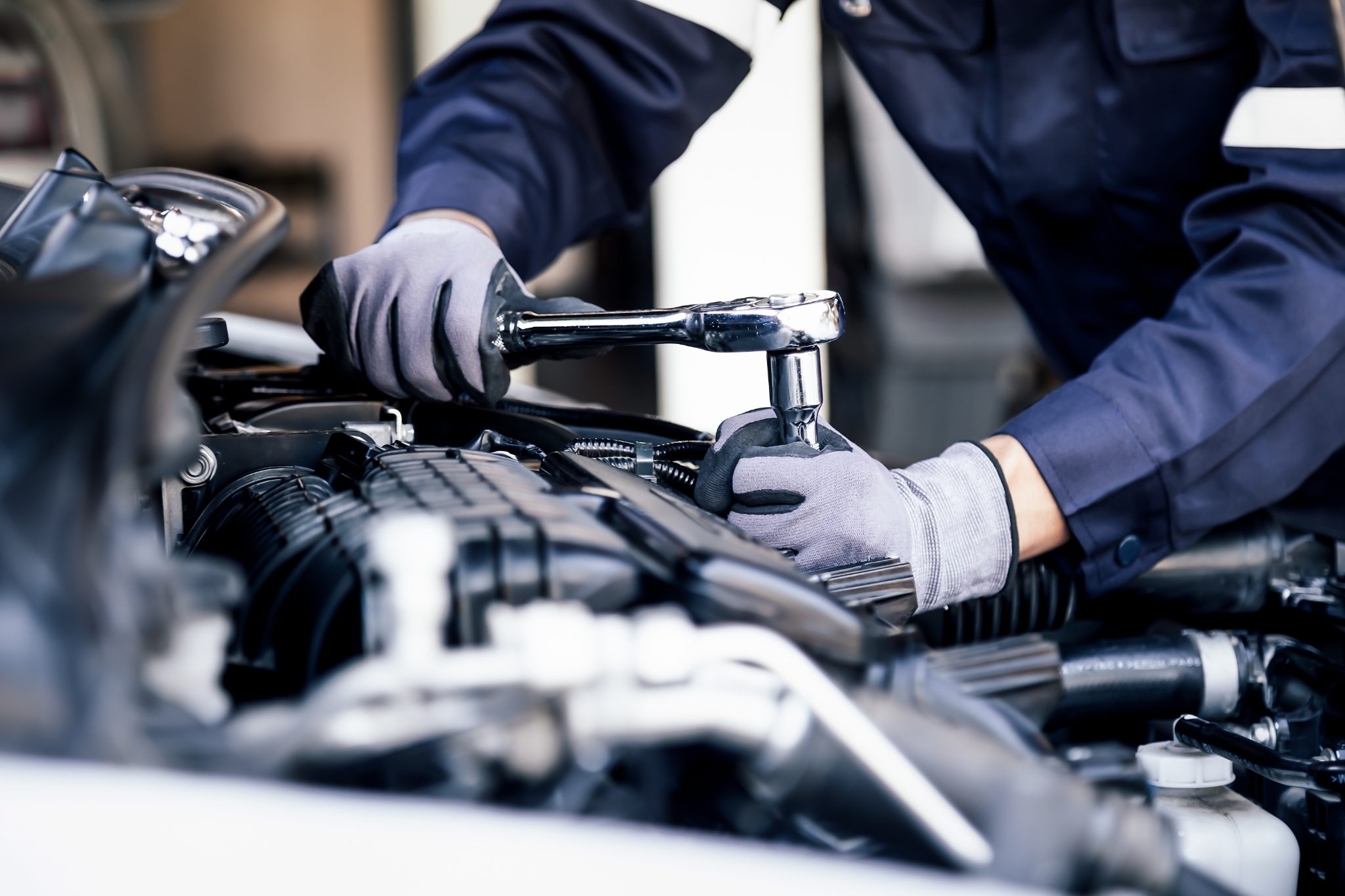 Mechanic in blue uniform and white gloves using wrench on engine component