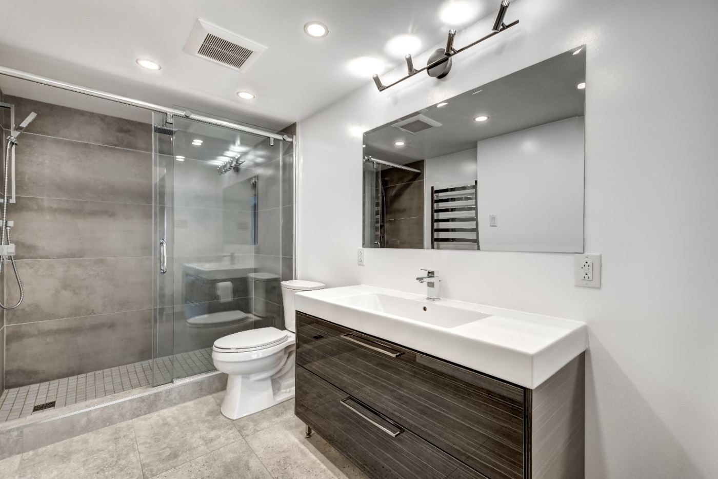 Modern bathroom with white vanity, glass shower enclosure, and gray tile flooring