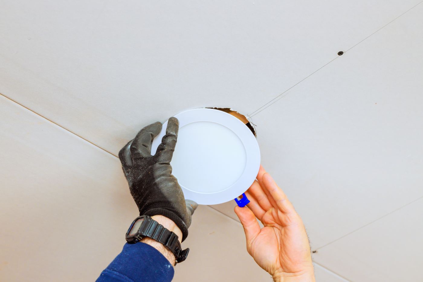 Worker installing recessed ceiling light fixture with gloved hands