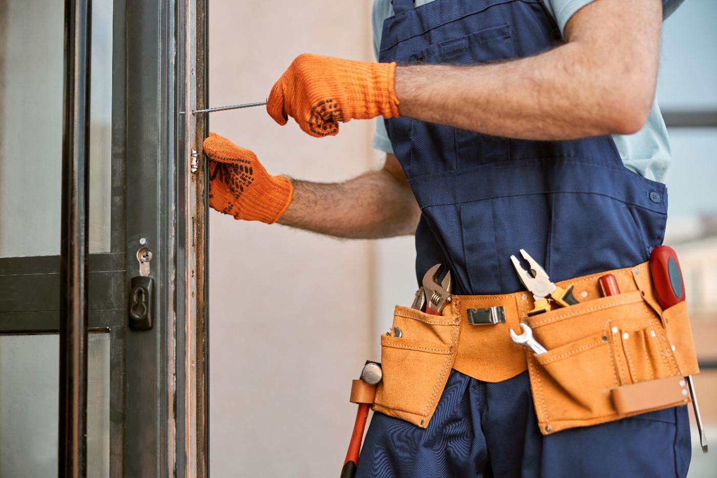 Tradesman in orange gloves and tool belt adjusting door lock with screwdriver