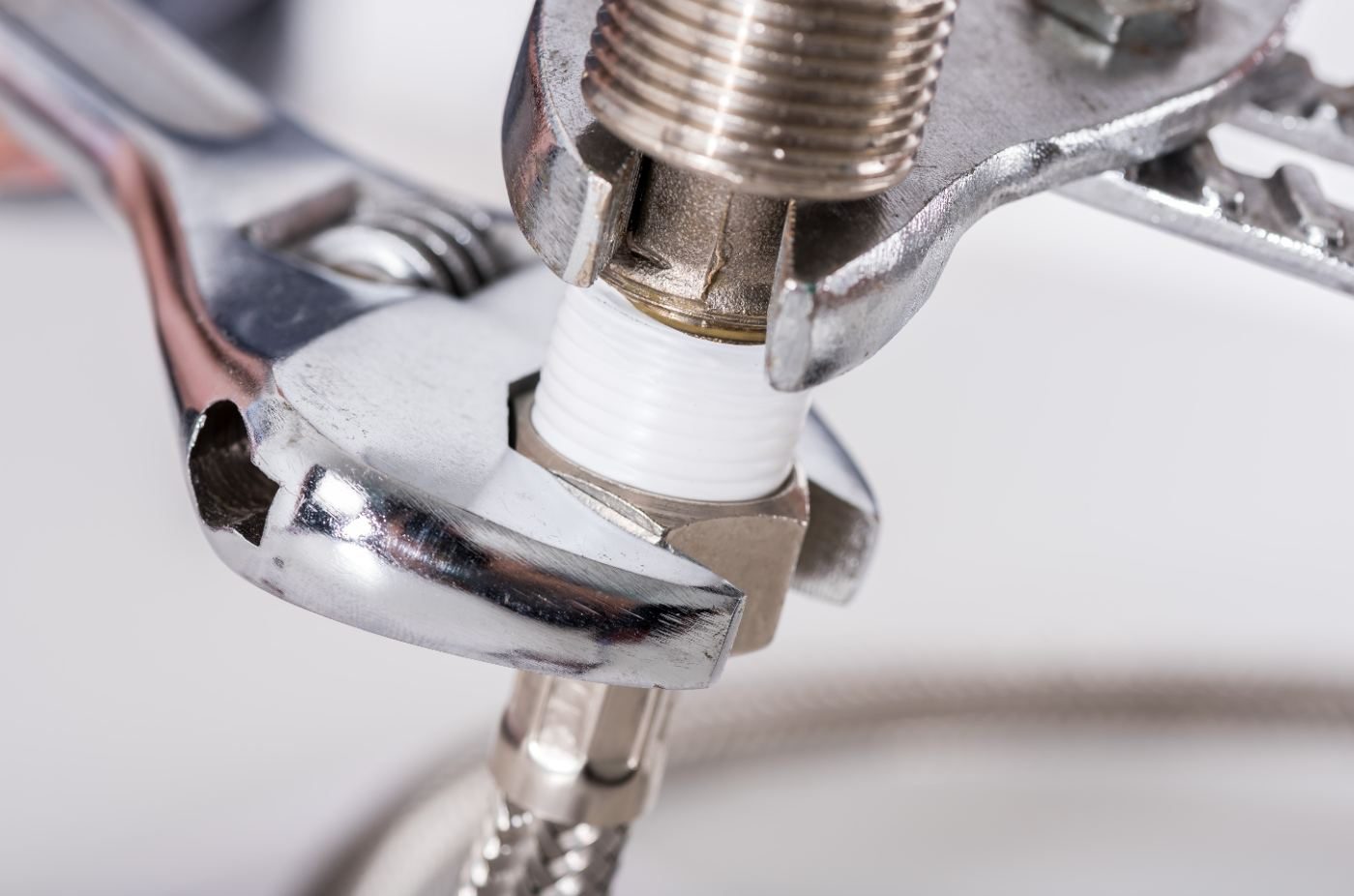 Wrench tightening a chrome fitting with white Teflon tape on plumbing connection
