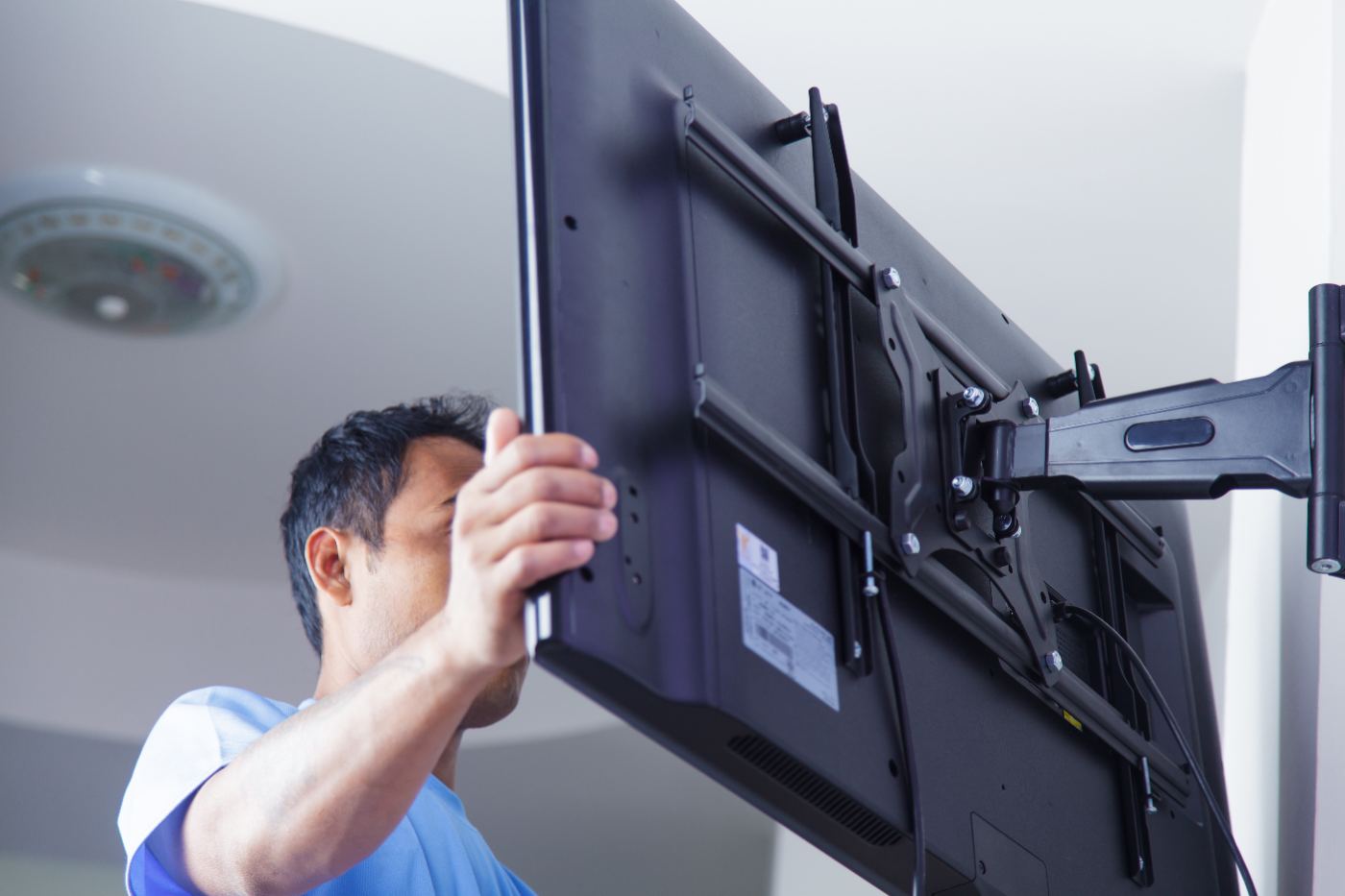 Technician in blue shirt installing flat screen TV on wall mount bracket